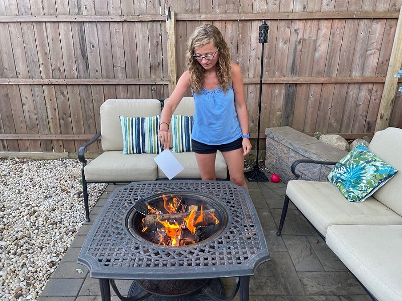 Me in shorts and a tanktop holding a photograph above a fire pit.