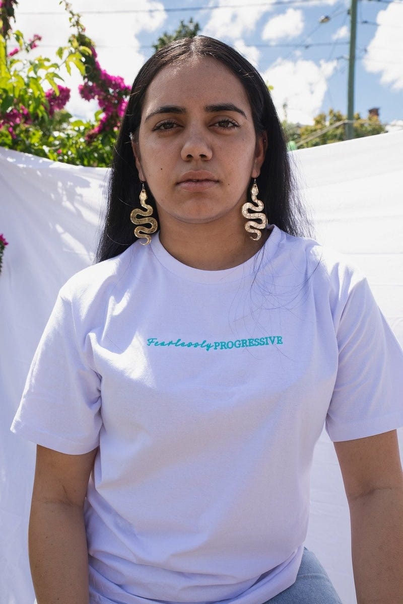 A person is wearing a white t-shirt with ‘Fearlessly Progressive’ written on the chest in blue writing.