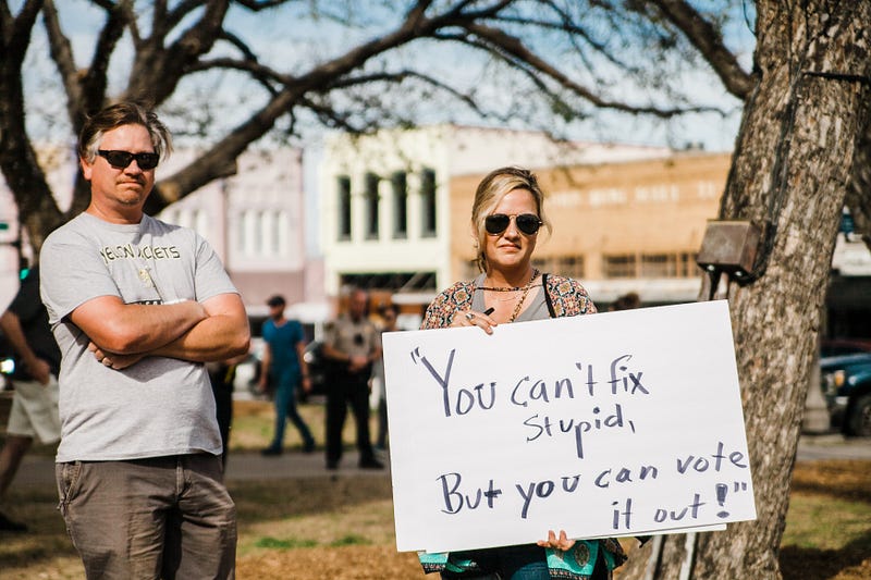 woman holding sign saying you can’t fix stupid but you can vote it out