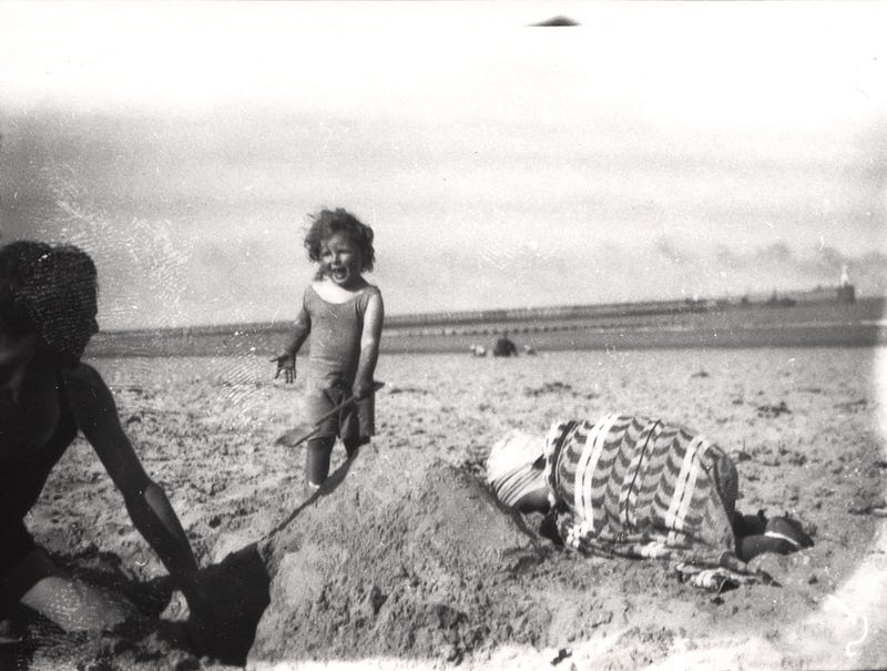 A child laughs, playing on a beach in the 1930s, her wind blowing in the hair.