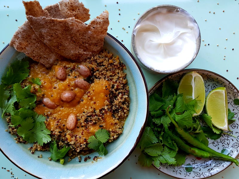 A bowl with a carrot and potato soup, served with beans and quinoa