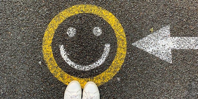 Person’s feet standing next to a smiley face stenciled on the pavement.