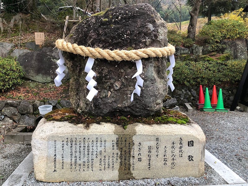 Sazare-ishi at Izumo Daijingu Shrine in Kameoka City, Kyoto Prefecture. The lyrics of “Kimigayo” (Japan’s national anthem) are inscribed on the stone’s base (Author’s photo))