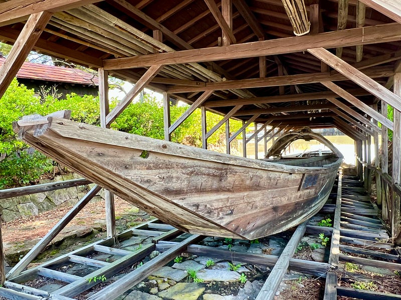 Long, narrow wooden boat under a wooden roof. Sakata, Yamagata.