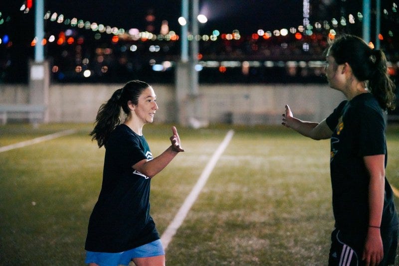 Two women on a playing field move to high five each other