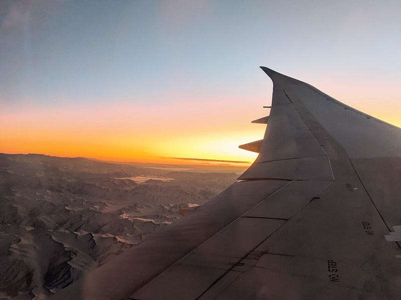 A picture of an airplane wing while flying over a mountain at daybreak