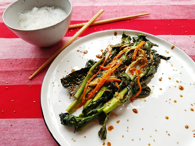 A plate with fried asian greens, next to a bowl of rice
