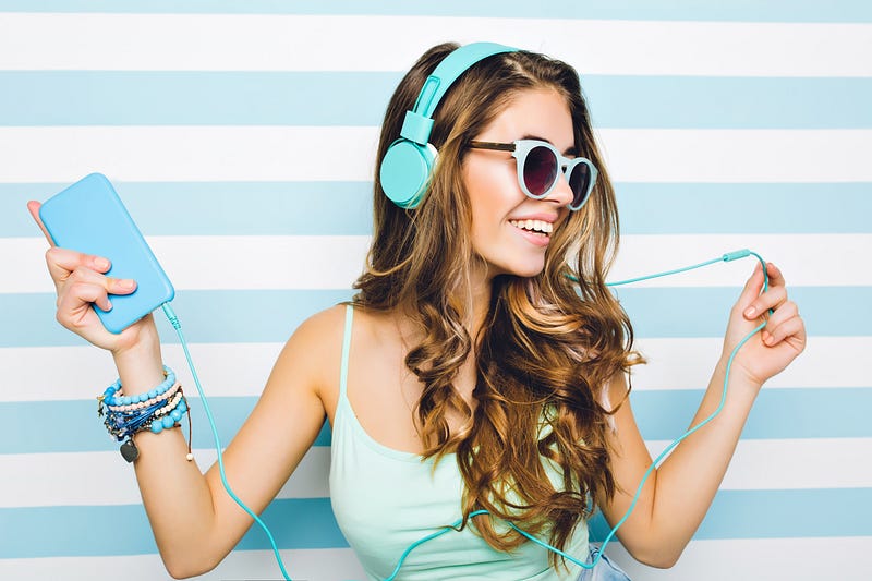 Young woman with sunglasses and headphones is dancing to music.