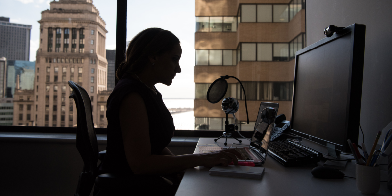 A dark silhouette of a woman working at a dimly-lit desk