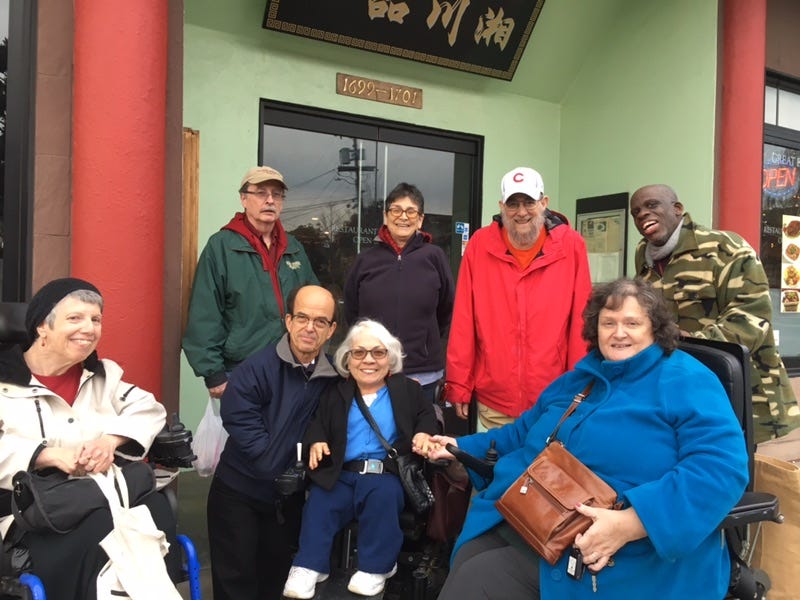 Celebrating Winter holidays at a Chinese restaurant in Berkeley, CA in Dec. 2017. Standing in back are Eric Vance,, Jessica Hopkins, Steve Brown and Leroy Moore. Sitting in front: Valerie Vivona, Ann Cupolo Freeman. Standing to Ann’s left is her husband, Sam Freeman. Sitting at the right end is Lillian Gonzales Brown. Photographer, Mary Lee Vance. Everyone is smiling and Lil and Ann are holding hands. Everyone is warmly dressed with coats and jackets.