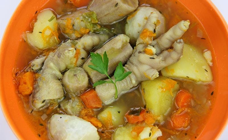 Close up of Jamaican chicken foot soup with carrots, yams, and green bananas, in an orange bowl.