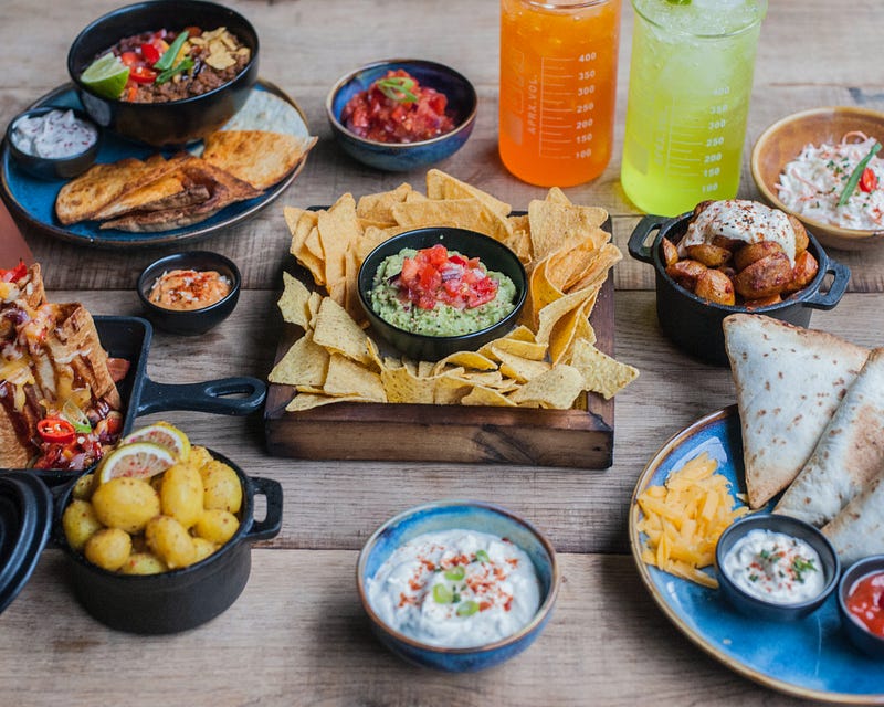 A table with nachos, salsa, drinks, and other lunch items.