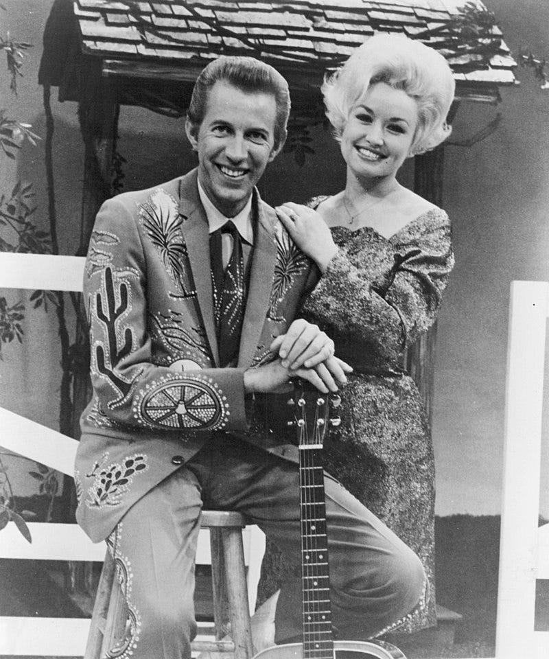 black and white, Porter Wagoner, seated, and Dolly Parton, standing to his left, hands on his shoulder, 1969