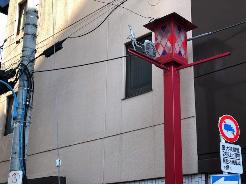 A lamp post that’s decorated with a rickshaw leading down to Yotsuya’s Sharikimon-dori
