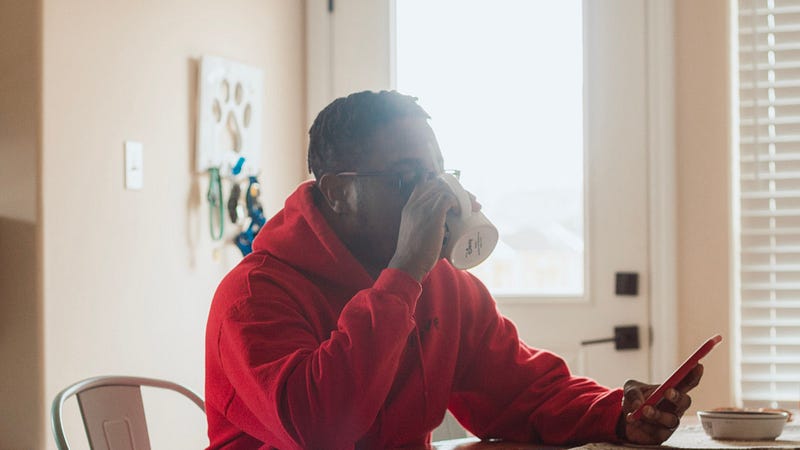 African American male in red hoodie sipping coffee and looking at smart phone.