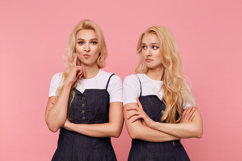 Watch Out, You May Have Two Accounts On Medium. Young brown-eyed long haired female keeping forefinger raised while looking attentively at camera, posing over pink background with her confused pretty blonde sister.