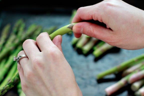 Image of a person breaking off the stringy part of an asparagus