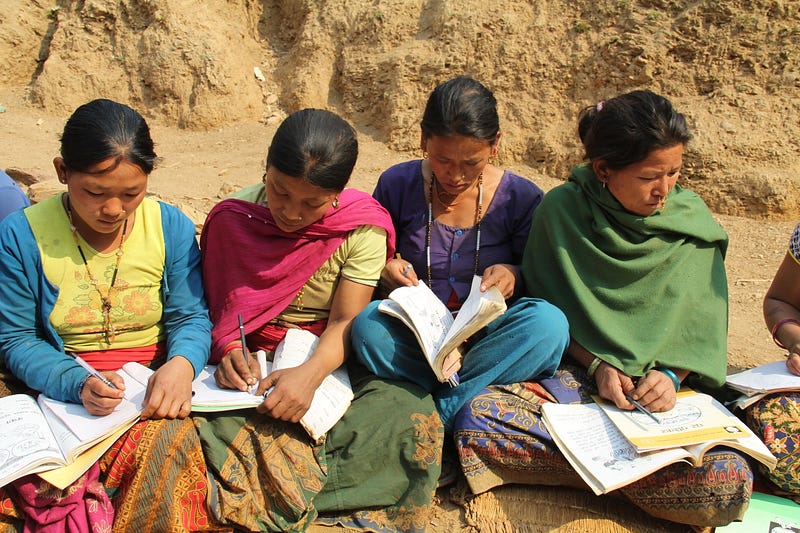 World Education Nepal Four Nepali women sit outside in a dirt field, writing in small notebooks