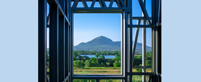 A photo of a lake and mountain through a steel-frame of an unfinished building