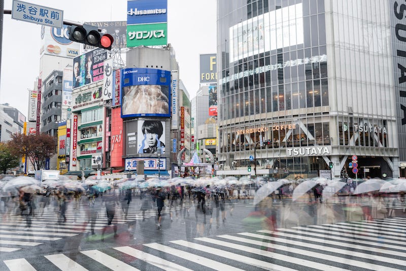 People with umbrellas cross Tokyo’s iconic Shibuya Scramble intersection during the rainy season