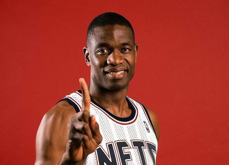 Dikembe Mutombo olha para a câmera e faz seu famoso gesto com o dedo indicador em riste, indicando que não vai dar chance ao adversário pontuar em cima dele