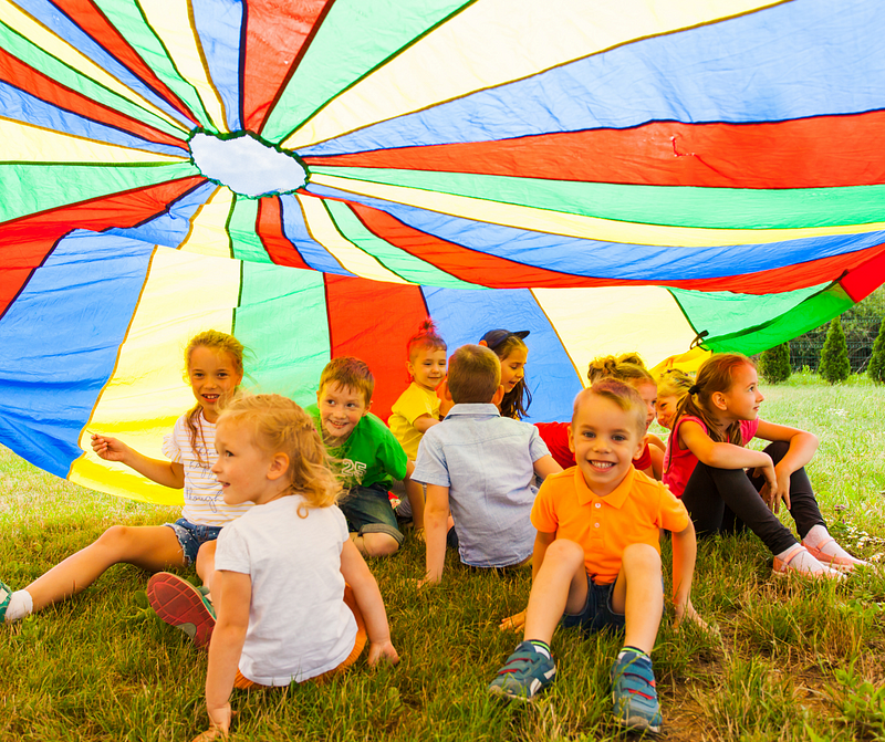 Primary school aged children sitting in a field underneath a coloured parachute.