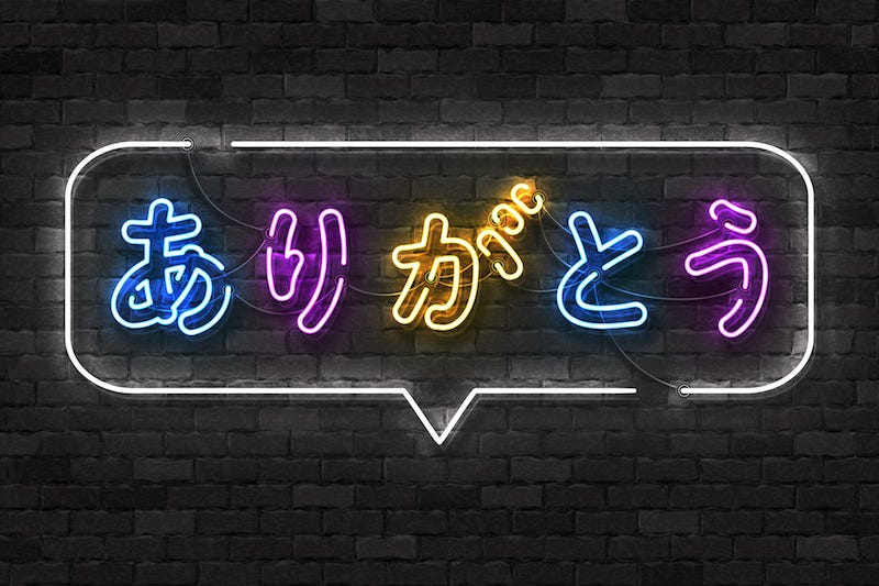A neon sign on a black brick wall reads “thank you” in Japanese