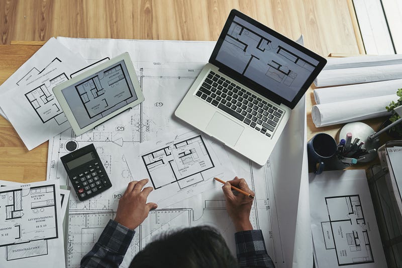 This image highlights the architectural planning process, featuring detailed floor plans, digital layouts on a laptop and tablet, and hands-on sketching by an architect. It reflects the perfect balance of traditional drafting and modern technology used in residential design projects. A true representation of professional architectural services focused on precision, functionality, and well-planned living spaces.