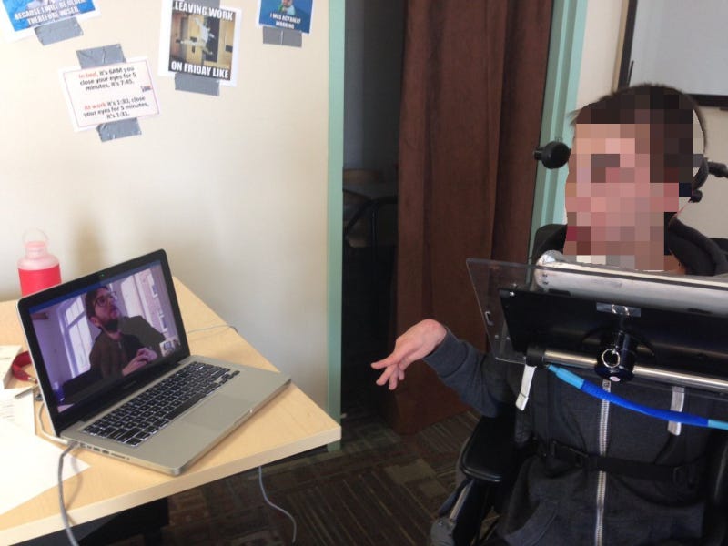 Remote usability testing, person in a wheelchair is looking at a screen with Dean looking back.