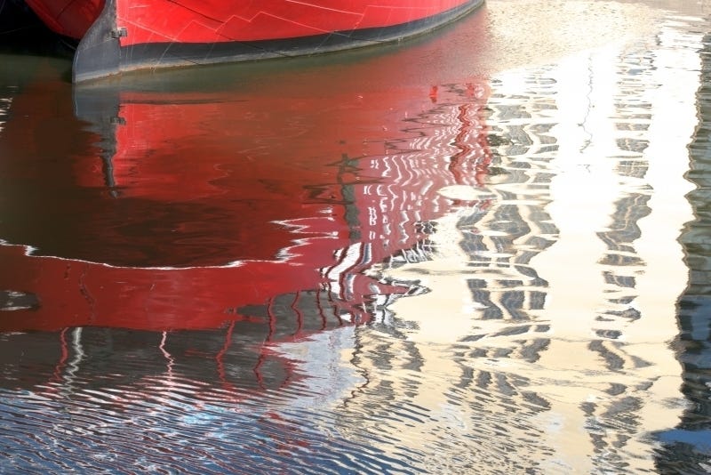 Abstract photograph of red boat in water with ripples and light reflection, for healing