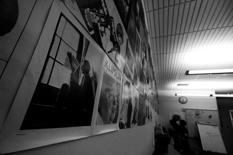 A wall covered in magazine spreads and the corner of the newsroom that contains a whiteboard and clock.