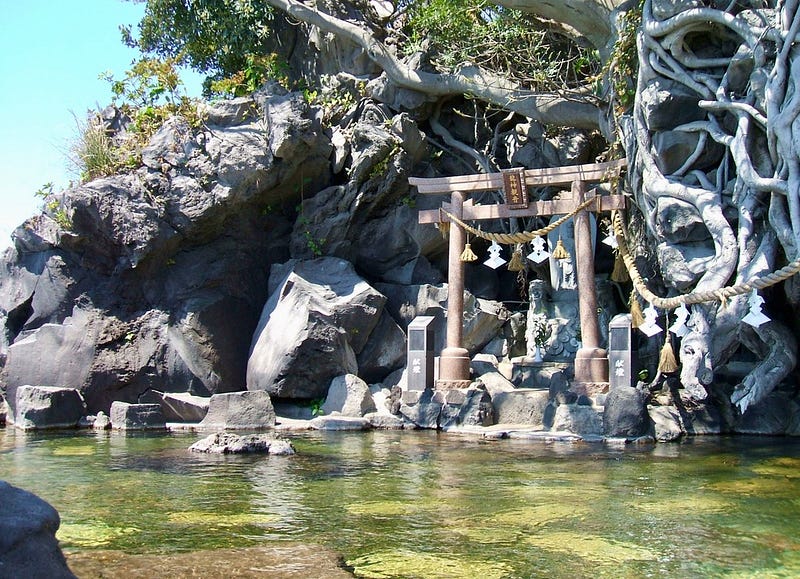 Hot springs with a torii gate, surrounded by volcanic rocks, climbing vines, and greenery.