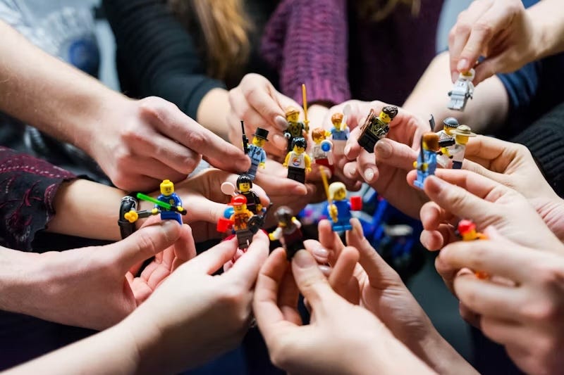A group of hands together each holding different lego figures.