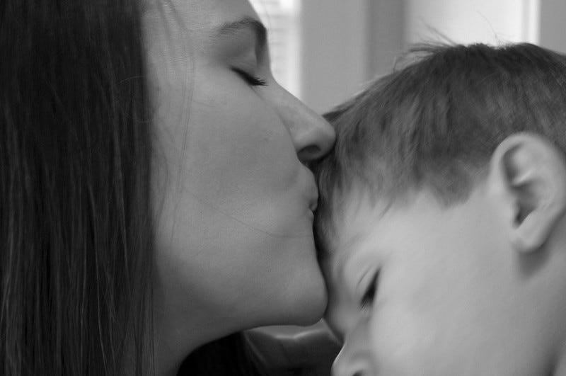 A mother kisses her young son on the forehead.