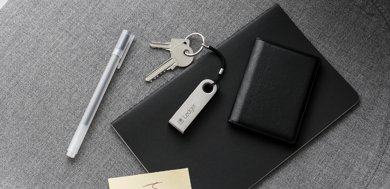 Ledger Nano S with keychain next to a wallet and notebook
