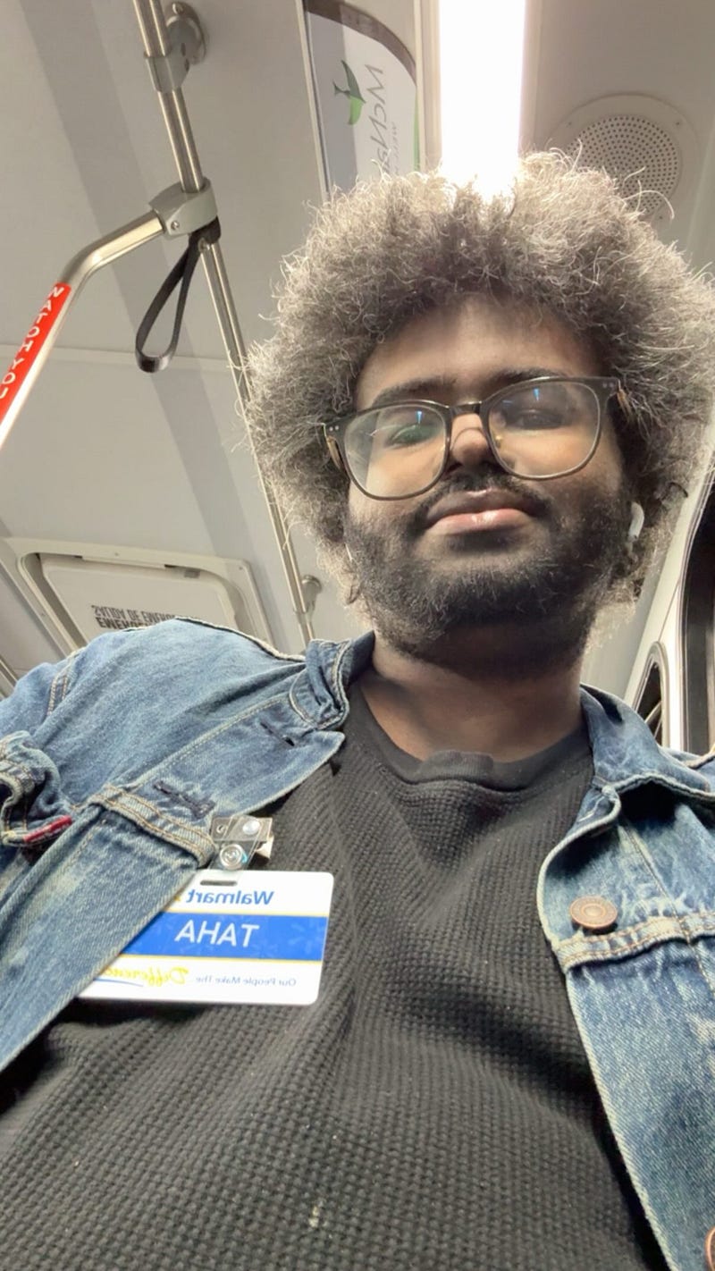 Looking fab on the way back from work at Walmart. I’m wearing a denim jacket and a black shirt. My name tag “Taha” with the Walmart logo is also shown.