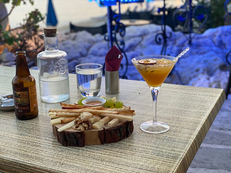 Cheese board with drinks around it and an ocean view in the background