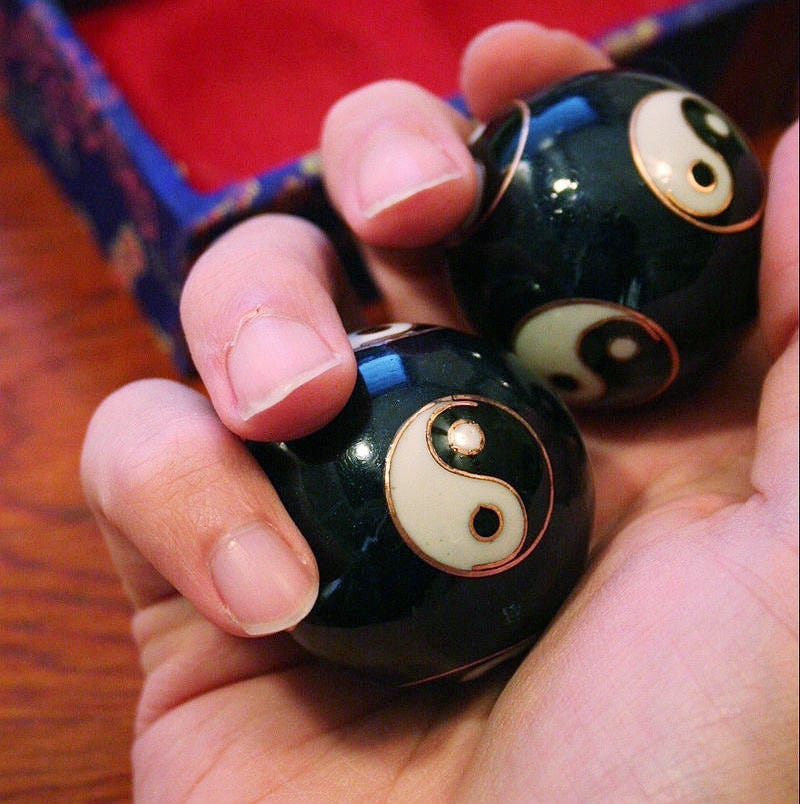 A hand holding a pair of baoding balls engraved with the Yin and the Yang.