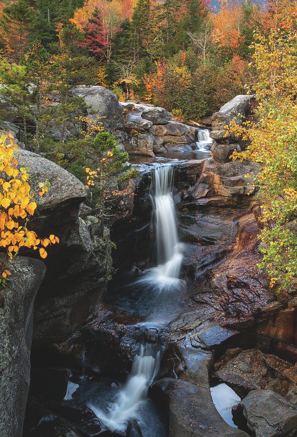 Screw Auger Falls in Maine flowing through rocky cliffs surrounded by brilliant red, orange, and yellow autumn leaves.