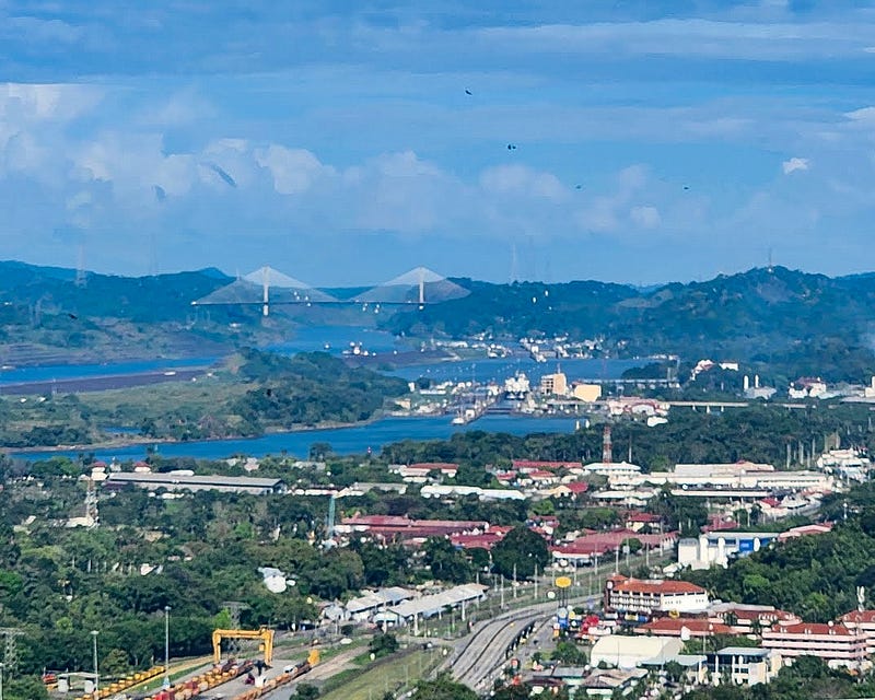 A shipyard and canal. Behind them a mountain range and large bridge. In the center the locks sit in the canal.