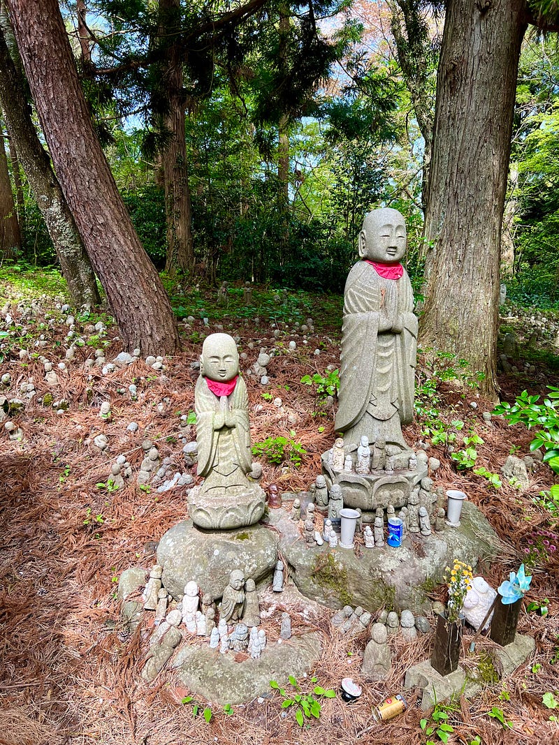 Two larger Jizō statues are surrounded by hundreds of smaller Jizō statues and gifts at the Nashi no Ki Jizō.