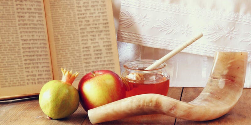 Image of items associated with the Rosh Hashana holiday: honey, an apple, a shofar horn, a pomegranate.