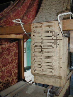 Folded punch cards draped over the side of a loom’s feed.