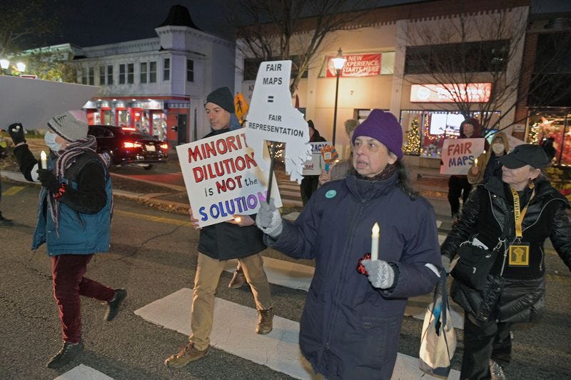 People in winter coats holding candles and signs (“Minority Dilution is not the Solution”, Fair Maps = Fair Representation”, “Fair Maps”) as they march through downtown Towson. (photo by Kenneth K. Lam/The Baltimore Sun)