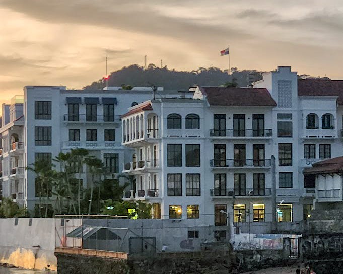 A mountain peak with a large Panamanian flag at the top in the background juts above Spanish Colonial style white hotels.