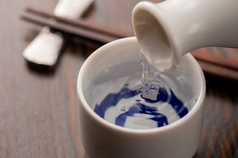 A person pours nihonshu into a cup at a Japanese restaurant