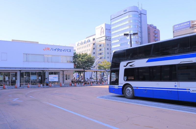 A highway bus sits outside of a major train station in Japan