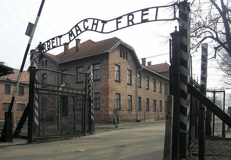 A picture of the entrance gate to the Auschwitz concentration camp in Poland. On top of the entrance, there is a sign made from metal letters that spell out Arbeit Macht Frei, which can be translated to English as Work Sets You Free. It is a slogan that is often used on the entrance gates to Nazi concentration camps. Picture is titled “Haupt-Eingangstor des KZ Auschwitz I, Arbeit macht frei (2007), Auschwitz, Polen” by Dnalor 01. Taken from Wikipedia Commons.