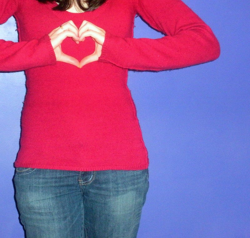 A woman holds her hands in the shape of a heart in front of her chest.