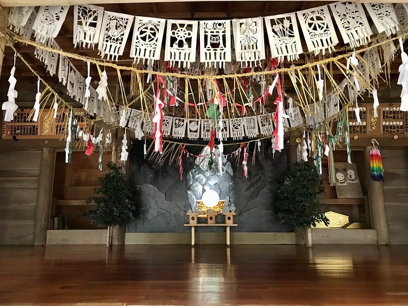 A shrine hall hung with paper and ropes, brilliant mirror on the altar.